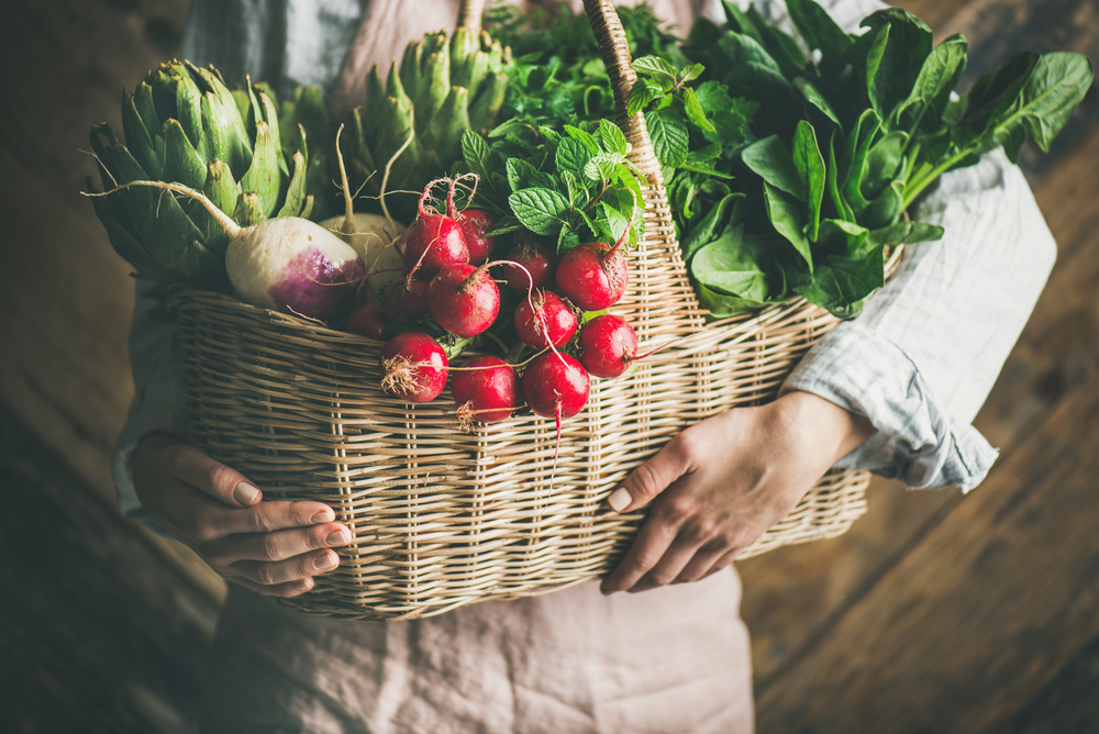 a woman holding a basket of fresh garden vegetables